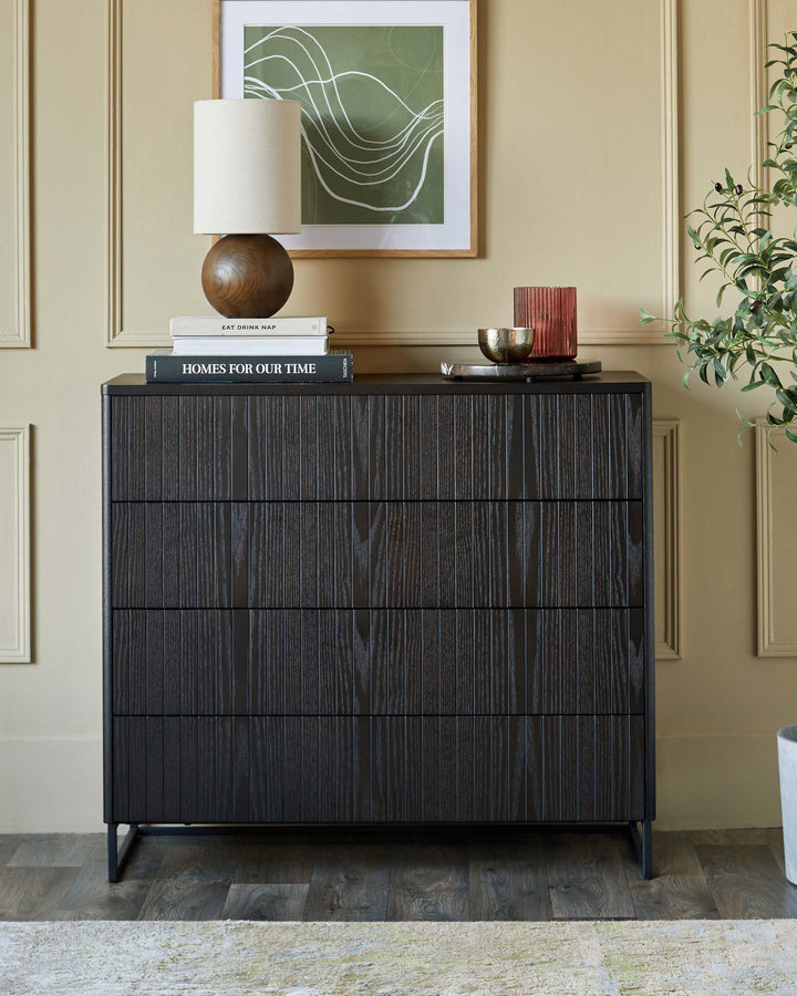 Dark wood chest of drawers with 3 drawers, styled with a lamp, books, and accessories. Neutral wall and rug provide a calm setting.