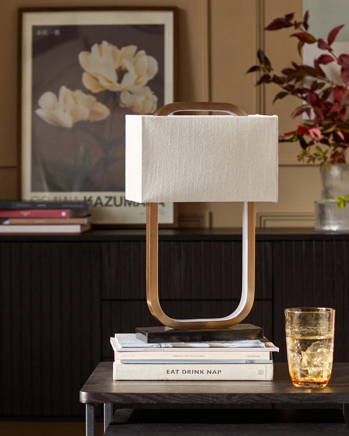 Stylish lamp atop stacked books, on a dark wood side table with a matching sideboard, exudes modern sophistication.