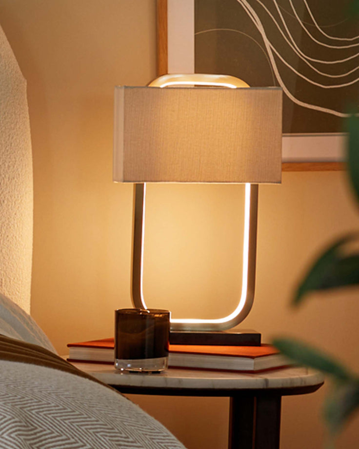 Bedside table featuring a lamp, books and a glass, all beautifully illuminated.