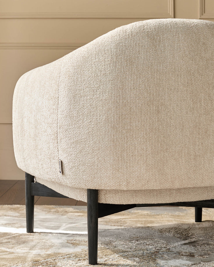 Close-up of a light-beige armchair with dark wood legs, showcasing its textured fabric and modern design.