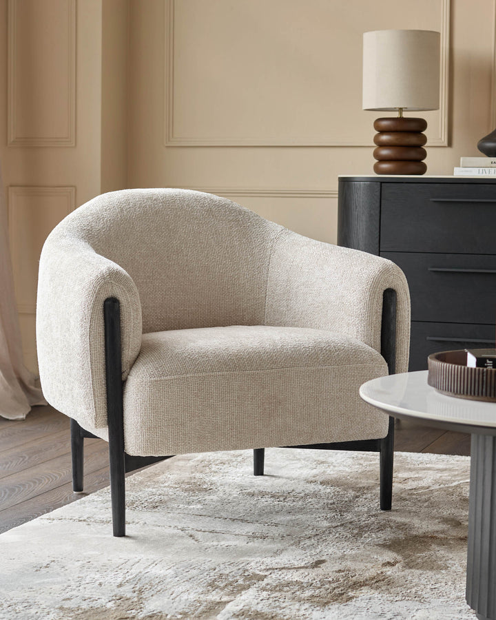 A stylish neutral armchair sits atop a patterned rug. A lamp and cabinet are in the background.