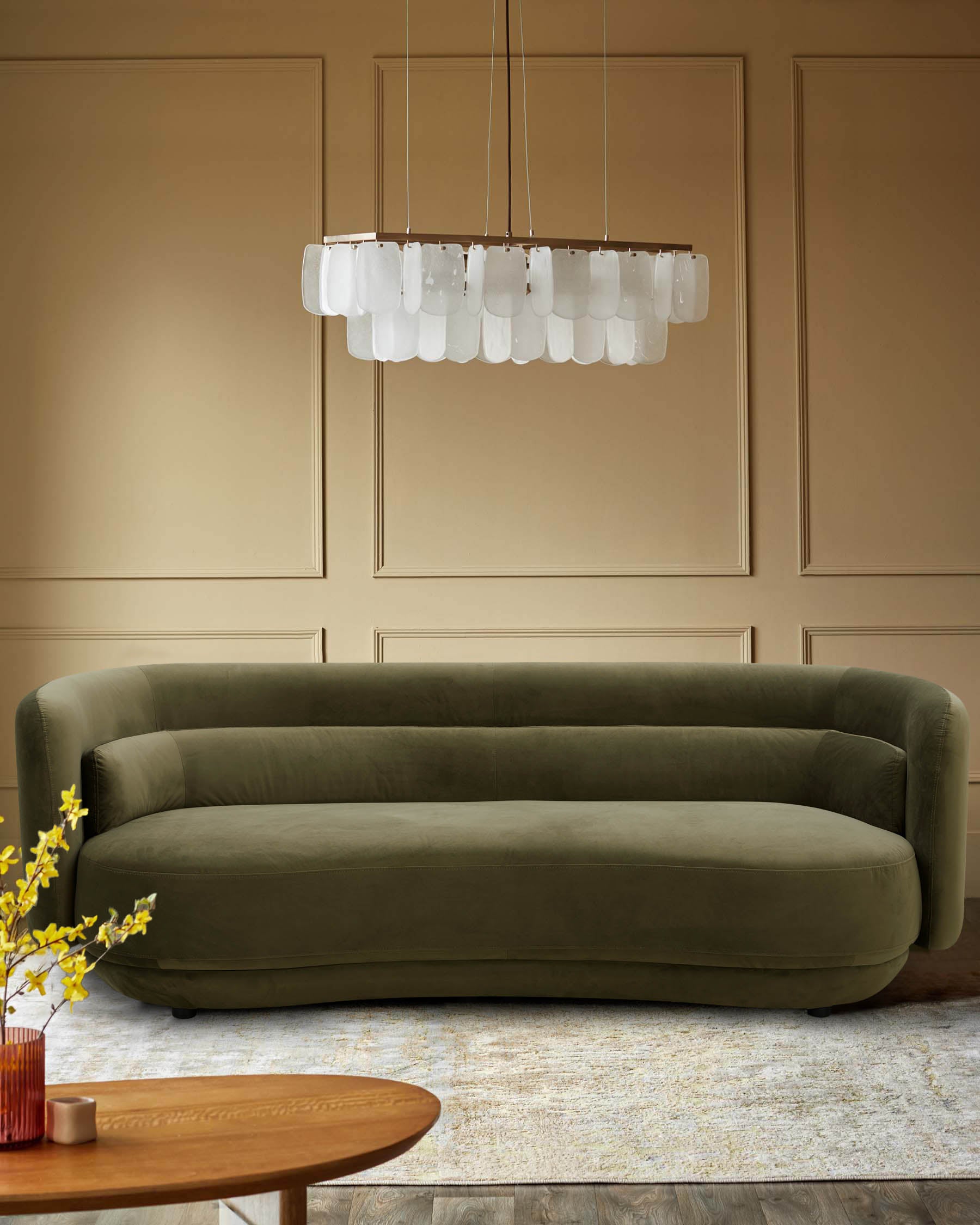 A modern living room with a green velvet sofa, statement lighting and a round coffee table with vase of flowers.