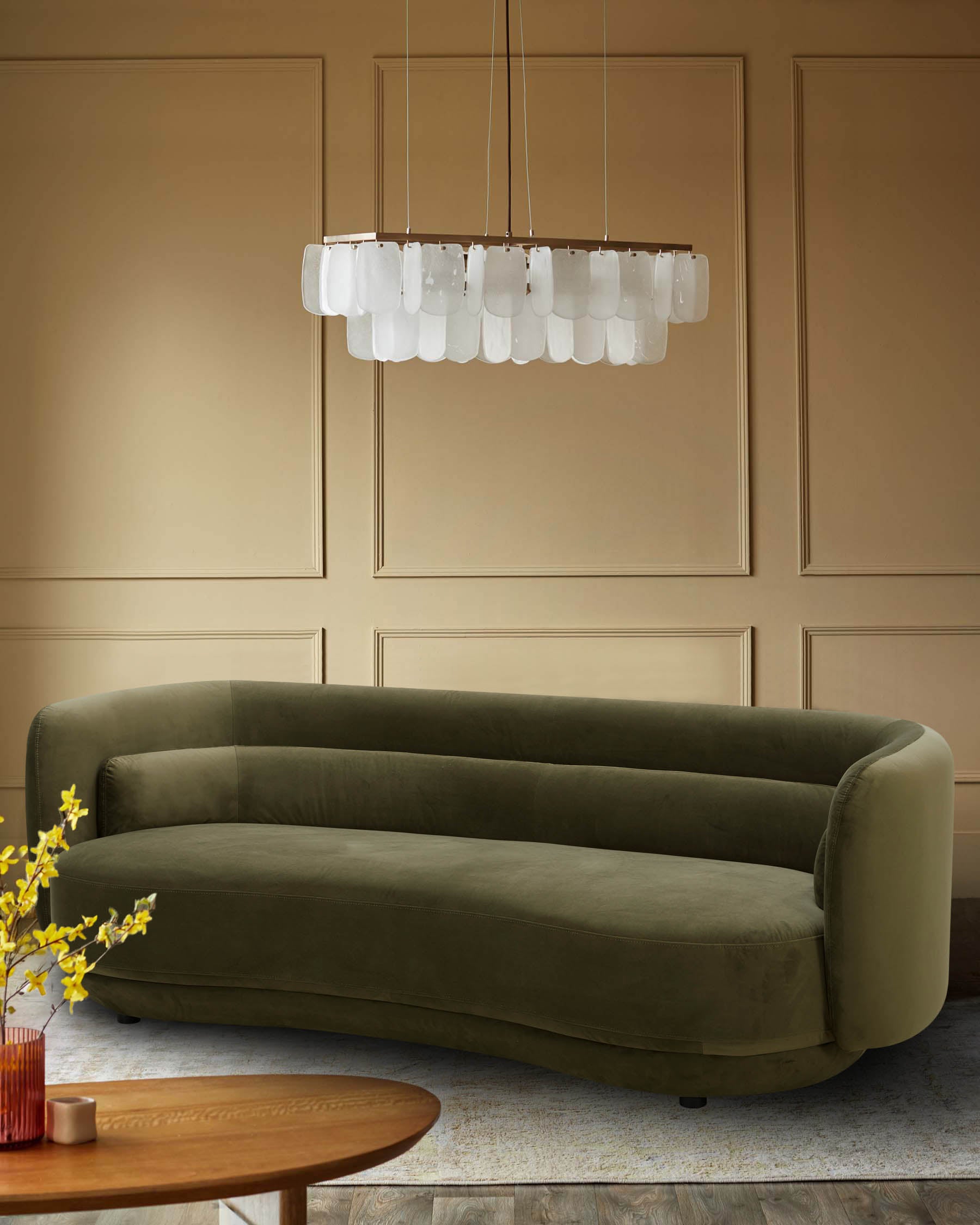 A stylish olive green curved sofa sits under a modern chandelier in front of a tan panelled wall.