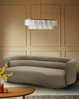 A beige, curved sofa sits beneath a modern, rectangular chandelier. A wooden coffee table is placed nearby.