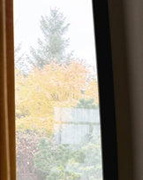 Black full-length leaner mirror reflecting autumn garden view with yellow foliage and evergreen trees.