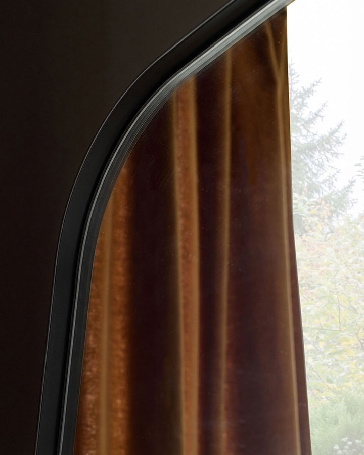 Caspian full-length leaner mirror with black frame, arched top detail, and window reflection view.
