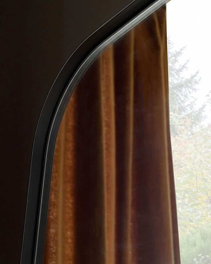Caspian full-length leaner mirror with black frame, arched top detail, and window reflection view.
