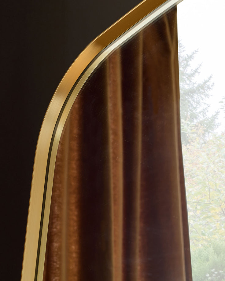 Channing full-length leaner mirror with gold frame and curved edge detail, angled view showing brown-toned reflection.