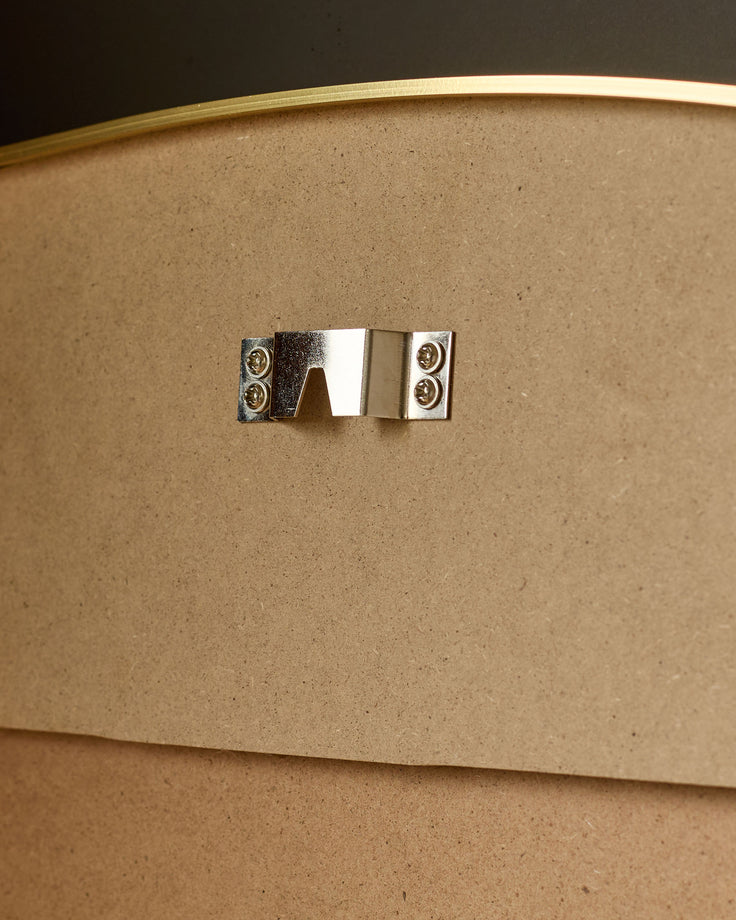 Gold framed leaner mirror showing polished metal handle detail on kraft cardboard backing.