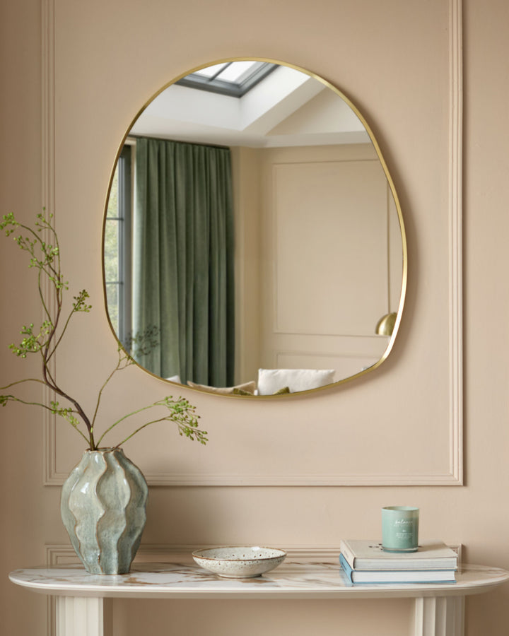 Gold-framed pebble-shaped wall mirror hanging above a marble console table with decorative accessories.
