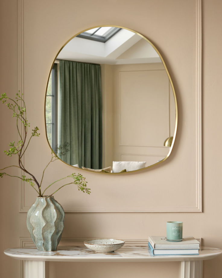 Gold-framed pebble-shaped wall mirror hanging above a marble console table with decorative accessories.