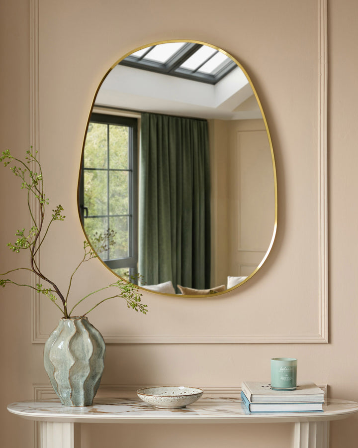 Gold-framed oval wall mirror with rounded edges, displayed above a marble console table with decorative accessories.