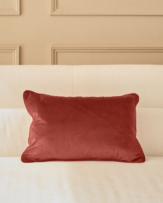 Luca rectangle cushion in toffee red velvet, displayed on a cream upholstered sofa against a paneled beige wall.