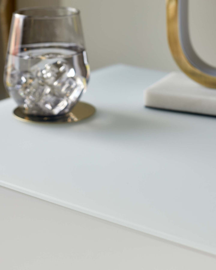Contemporary desk with a white surface, complete with a glass of water and stylish gold accents.