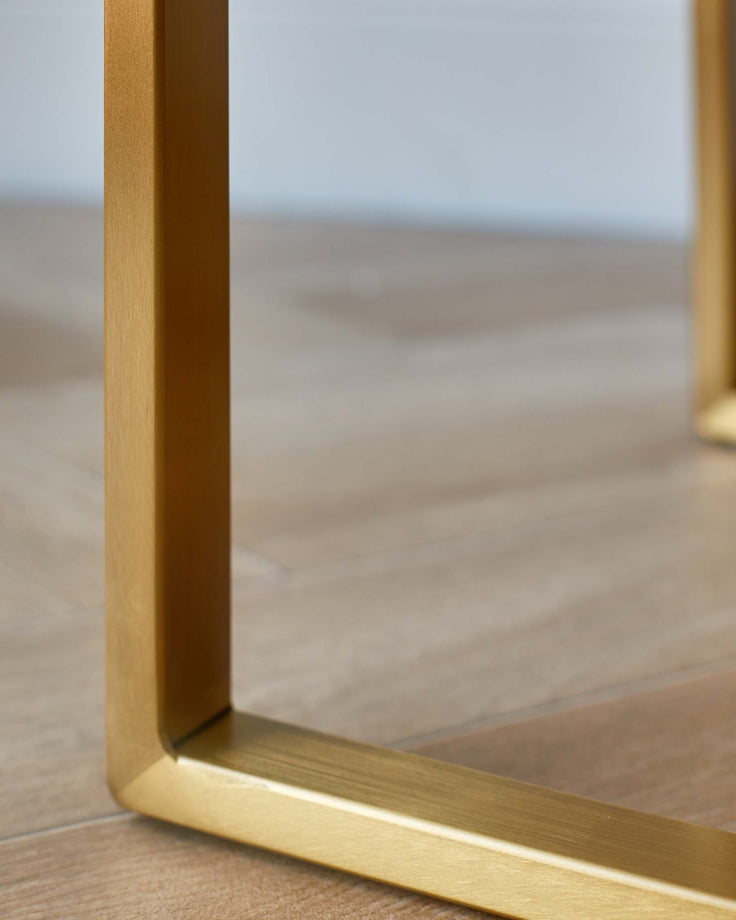Close-up of a gold, metal table leg on a wooden floor. Modern furniture with clean lines.
