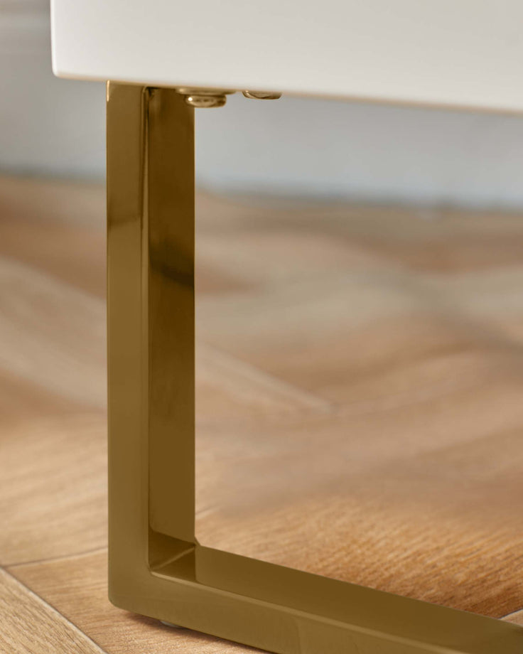 Close up of a white table or cabinet with a gold metal leg on a wood floor.