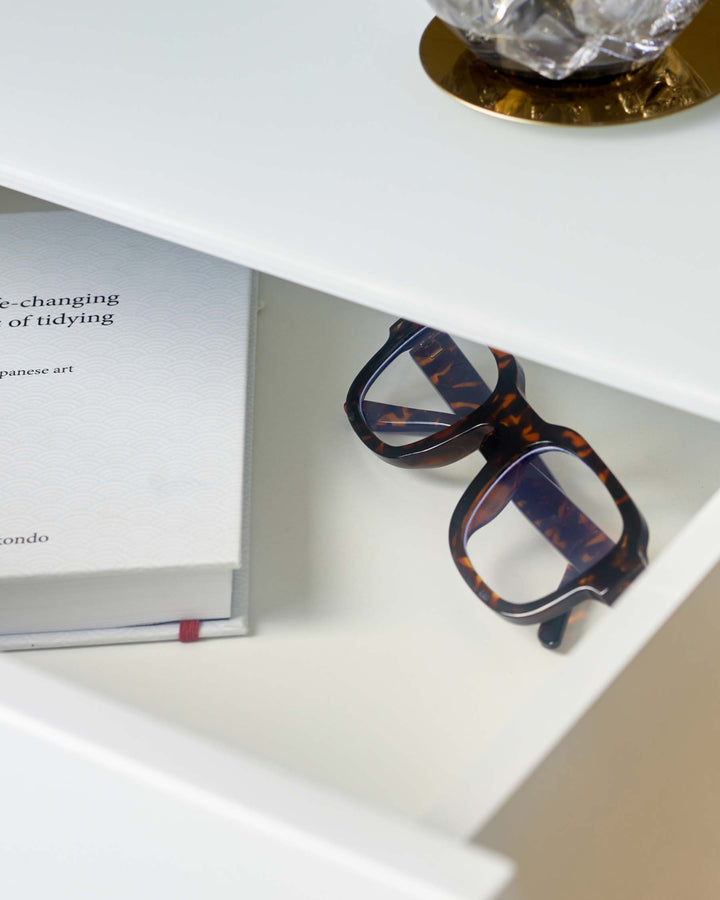 A white drawer with glasses and a book on display, showcasing sleek and modern furniture design.
