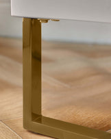 A modern side table leg in gold, against a wood floor. Part of a contemporary furniture design.