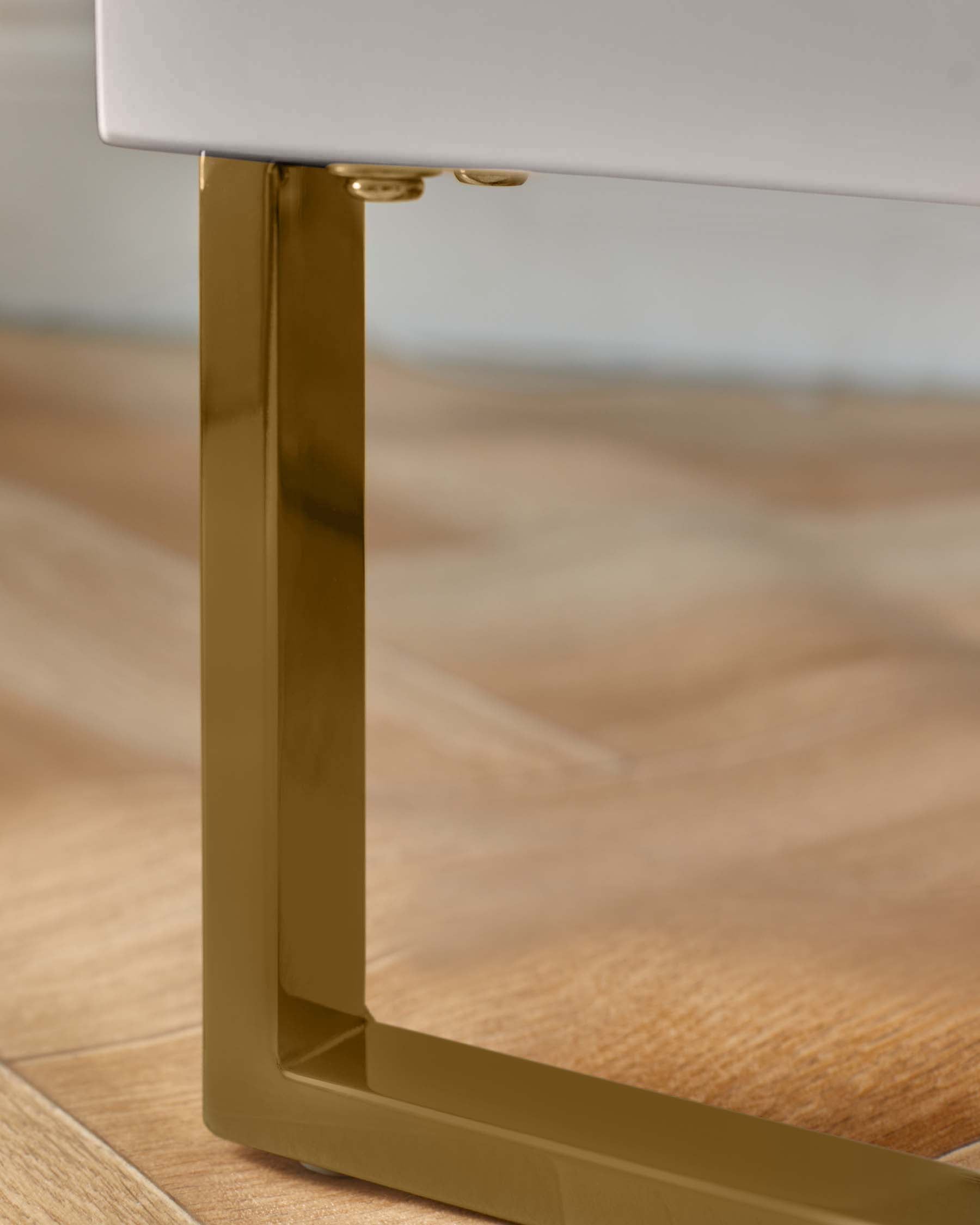 A modern side table leg in gold, against a wood floor. Part of a contemporary furniture design.