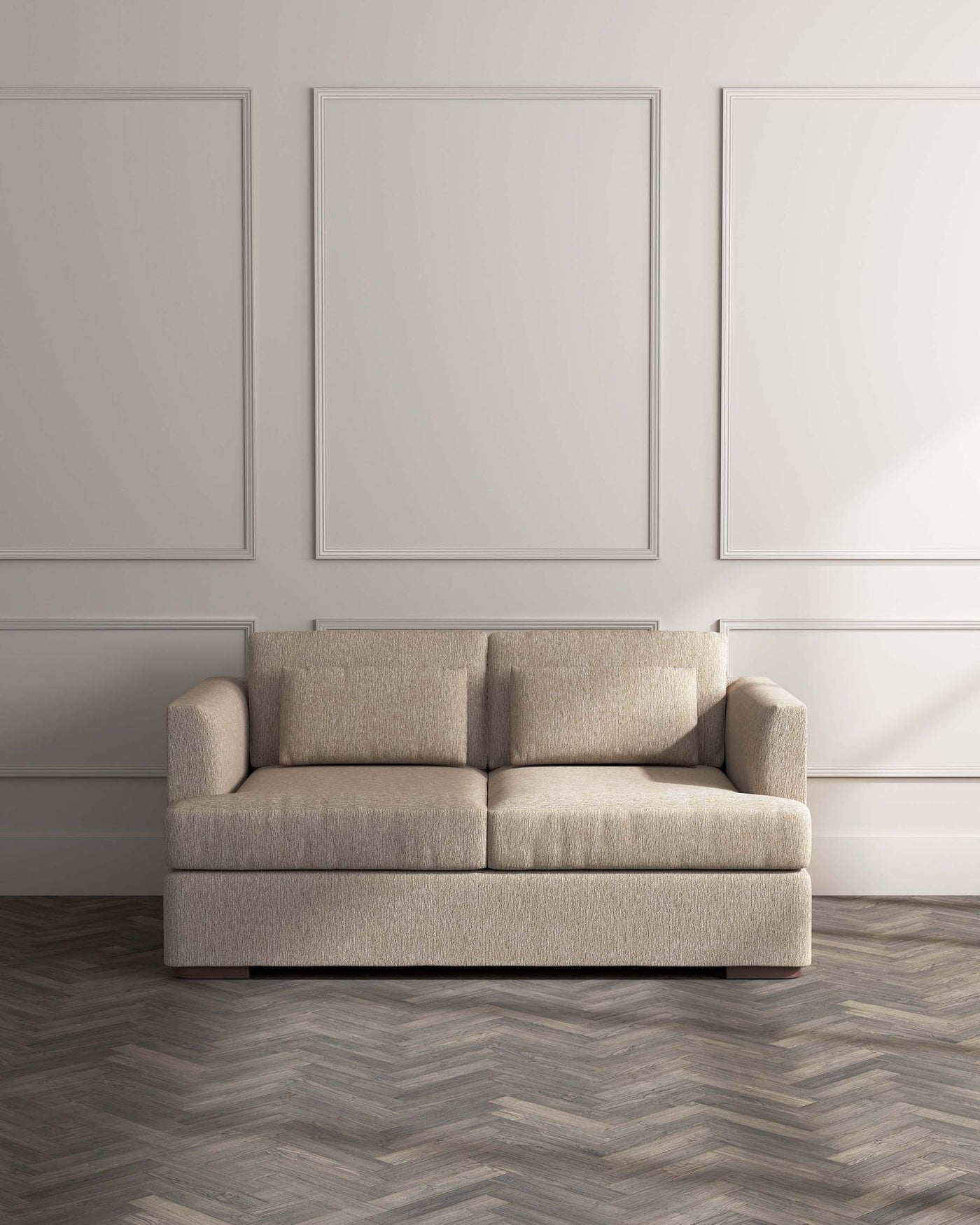 Modern beige three-seater sofa with clean lines and soft textured upholstery, positioned on herringbone parquet flooring against a wall with understated wainscoting and two framed decorative panels above.