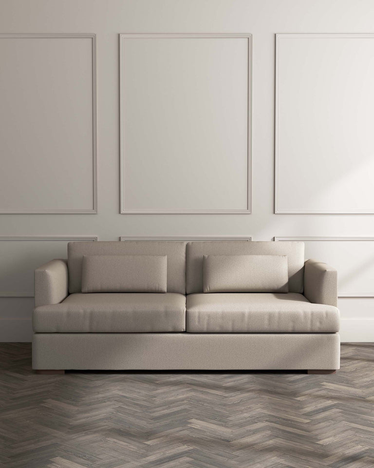 Contemporary three-seater sofa with a streamlined design and neutral beige upholstery, featuring clean lines, square armrests, and dark wood legs, set against a minimalist backdrop with framed art and herringbone-patterned flooring.