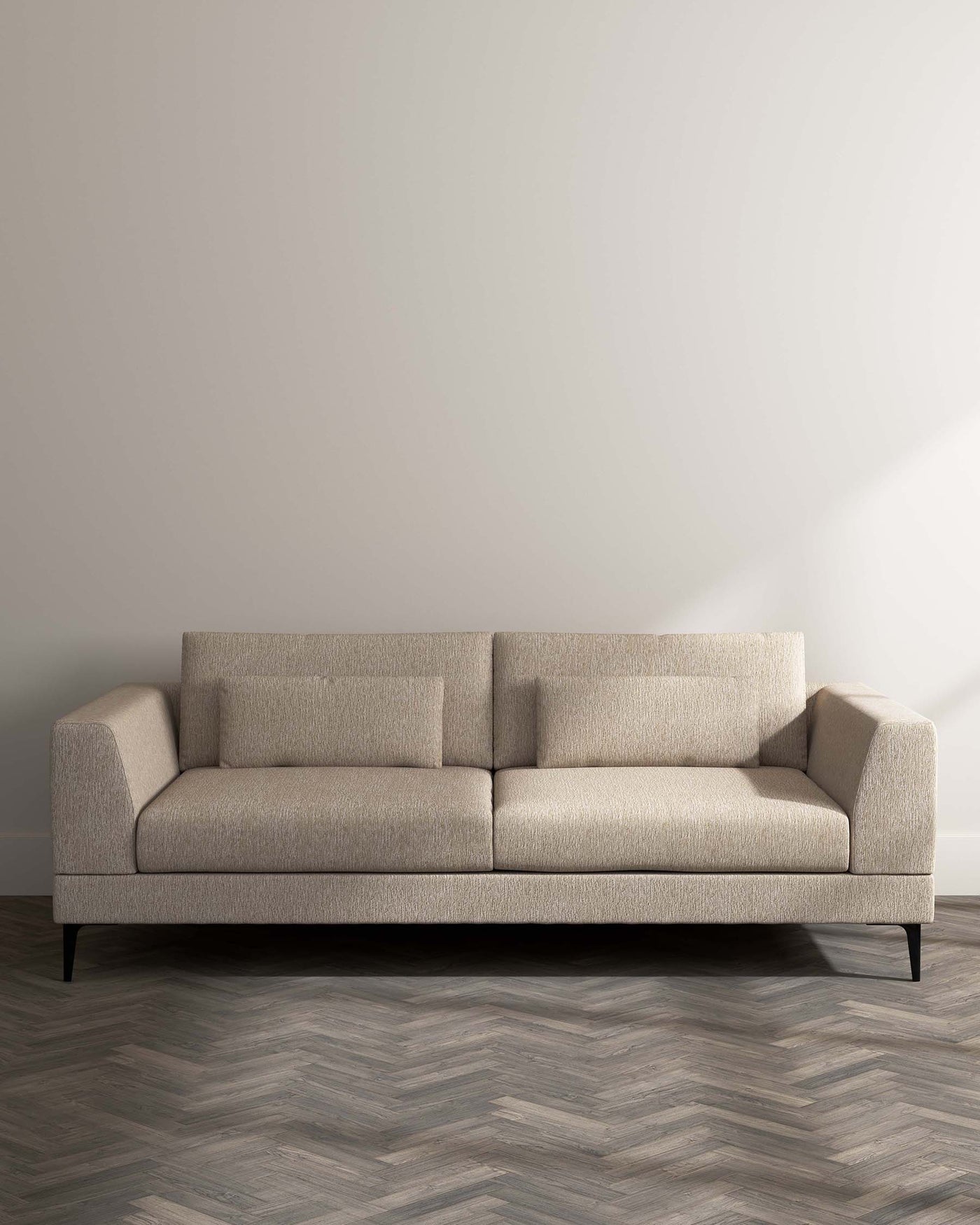 Contemporary three-seater sofa featuring a textured beige upholstery, clean lines, square arms, and tapered black legs. Positioned against a neutral backdrop on a herringbone pattern wooden floor.