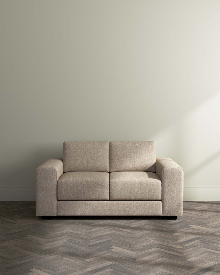Modern beige three-seater sofa with clean lines, plush cushioning, and a textured fabric upholstery. The sofa sits on a herringbone patterned wooden floor against a neutral wall, embodying contemporary elegance.