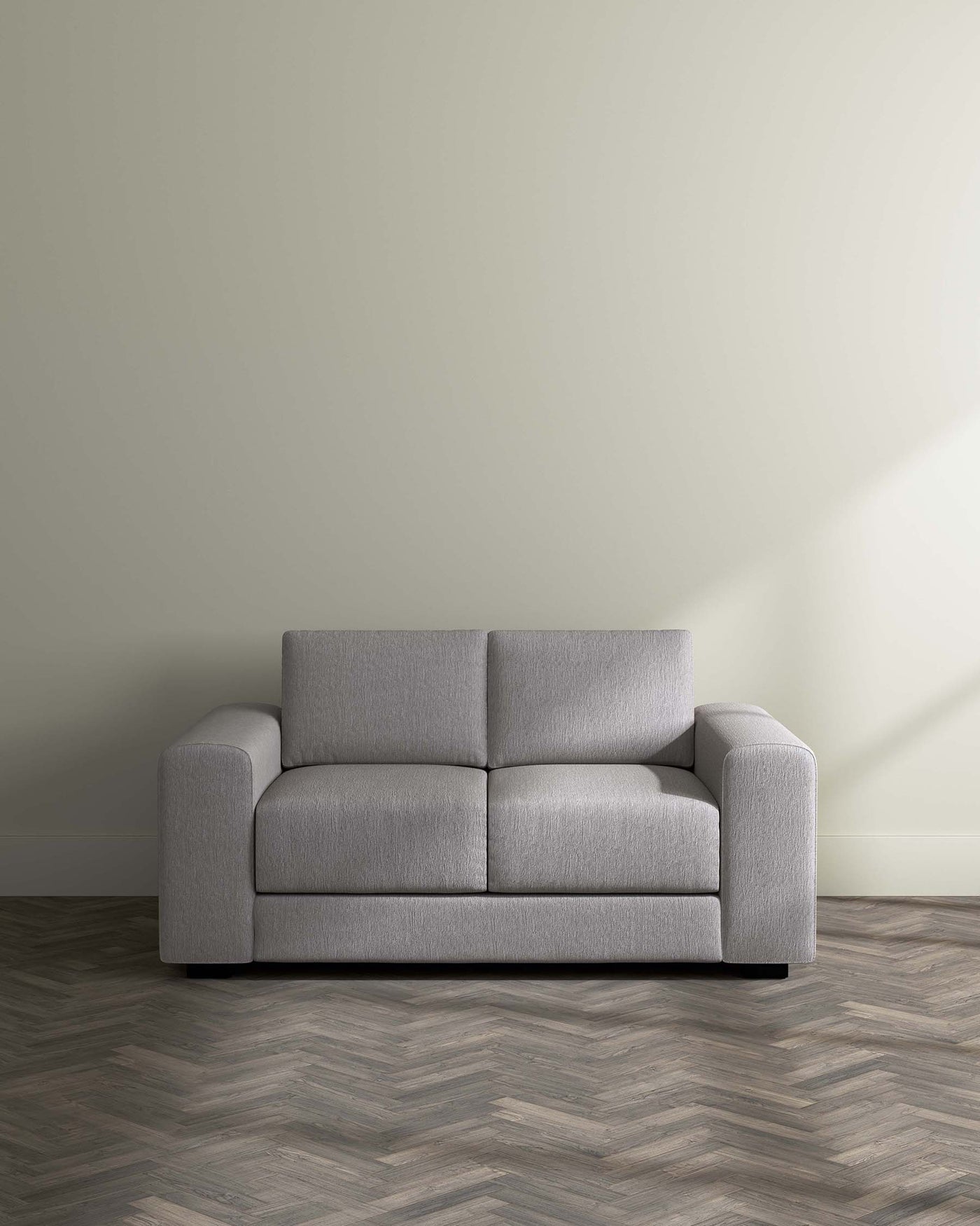 Modern light grey fabric sofa with clean lines and a minimalist design, featuring plush cushioning, wide armrests, and a low-profile silhouette set against a neutral wall on a herringbone-patterned wooden floor.