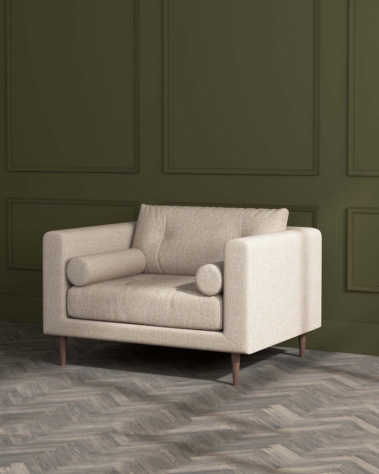 Modern beige fabric loveseat with clean lines, featuring plush back cushion, a deep seat cushion, two cylindrical side pillows, and angled wooden legs. Positioned in a room with elegant dark green panelled walls and herringbone patterned wood flooring.