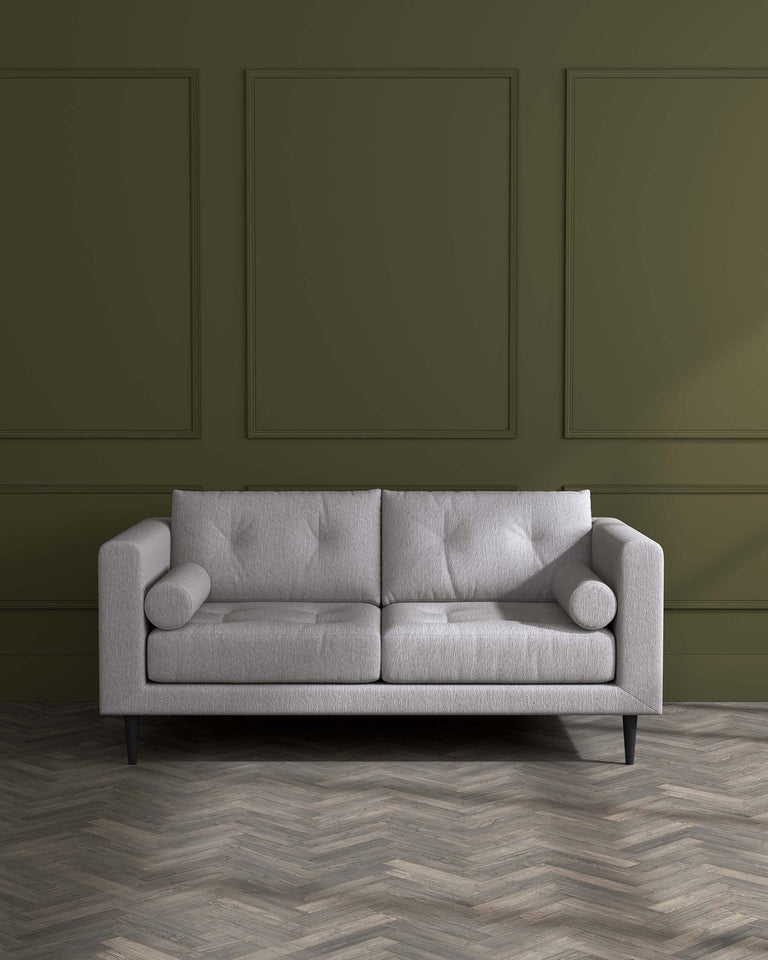 Modern three-seater sofa in light grey fabric with clean lines and minimalist design, featuring plush cushions, a tufted backrest, cylindrical side pillows, and sleek, tapered black legs.