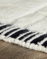 Close-up of black and white striped wool rug edge showing sculpted texture on wood flooring.