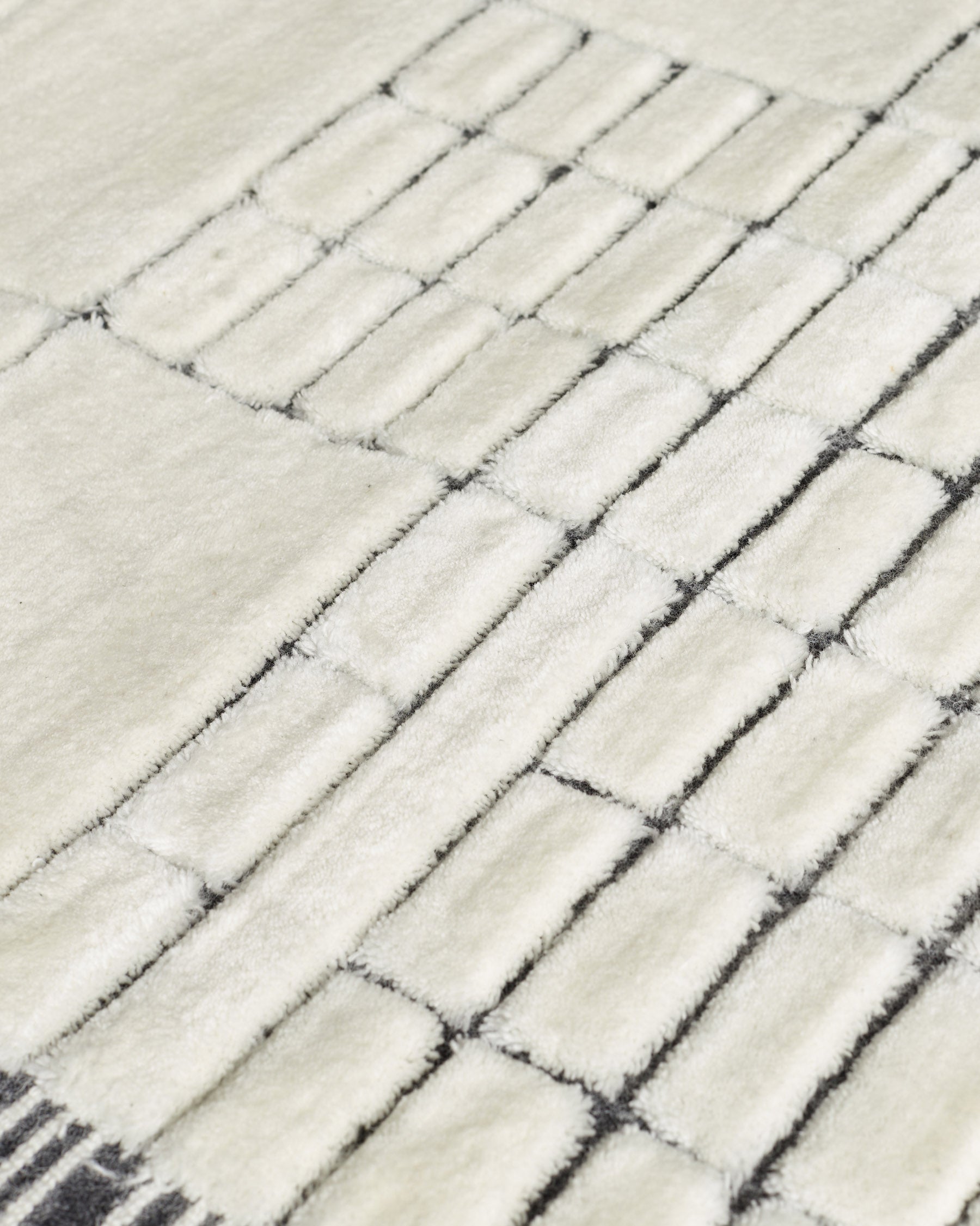 Close-up of medium sculpted wool rug in monochrome, showing textured herringbone weave pattern in cream and charcoal.