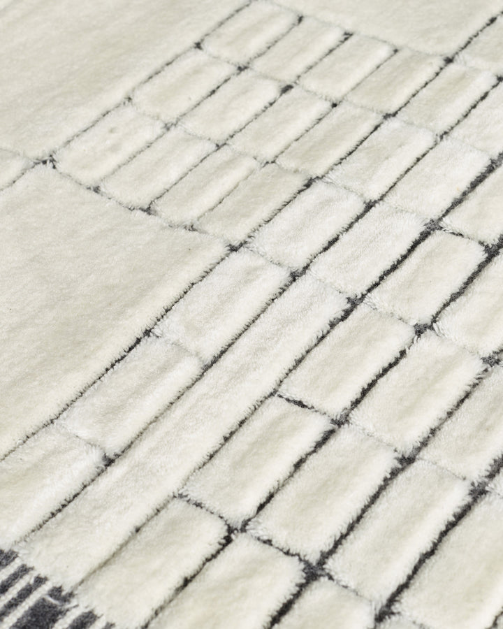 Close-up of medium sculpted wool rug in monochrome, showing textured herringbone weave pattern in cream and charcoal.