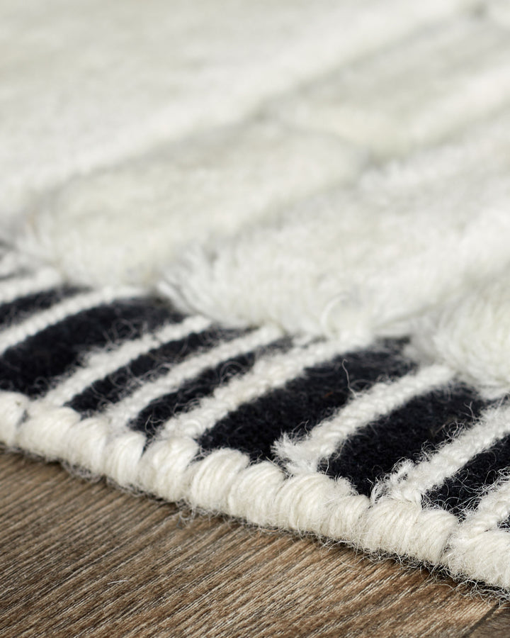Close-up of black and white striped wool rug edge on wooden floor, showing texture and woven detail.