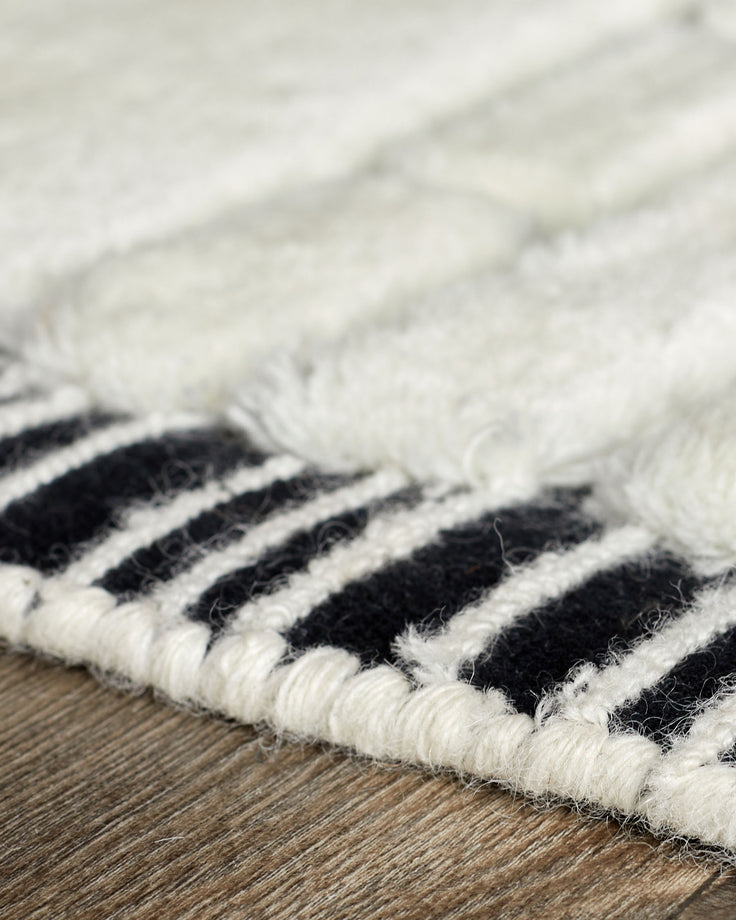 Close-up of black and white striped wool rug edge on wooden floor, showing texture and woven detail.