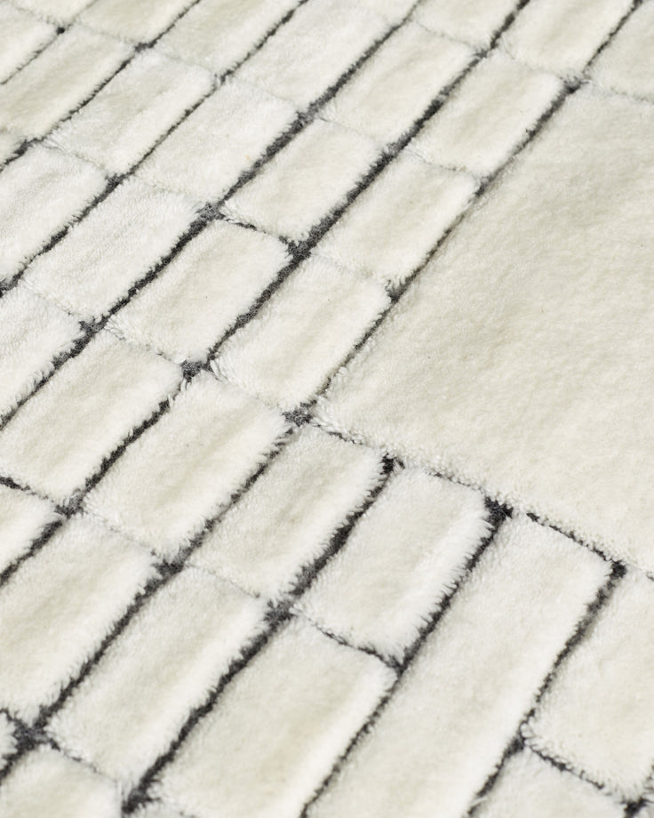 Close-up of mosaic large sculpted wool rug in monochrome, showing textured rectangular blocks in cream and charcoal.