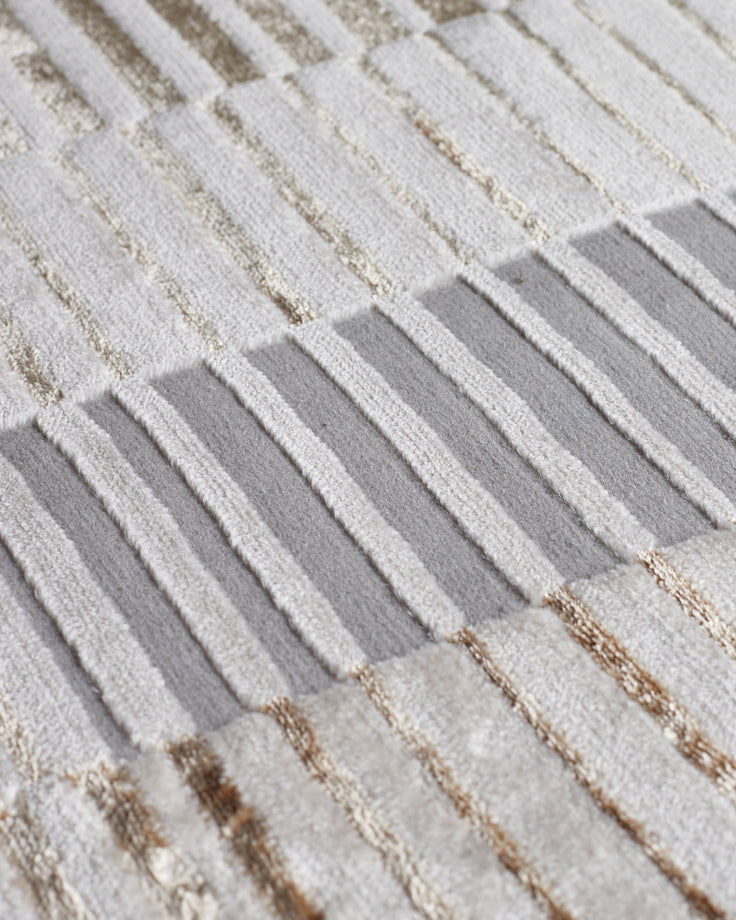 Close-up of textured rug showing cream and gray striped pattern with metallic thread details.