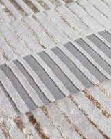Close-up of textured rug with white, gray, and beige stripes and woven metallic accents.