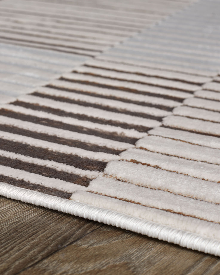 Bijou small textured rug in mixed metallics, showing striped pattern in cream, brown, and metallic tones on wood floor.