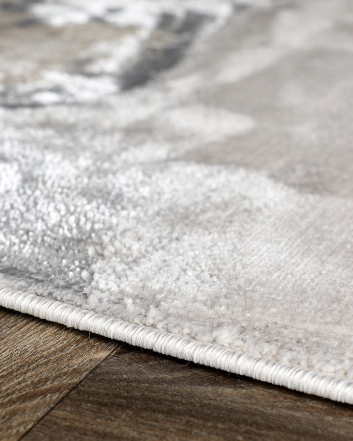 Perla medium textured rug in soft silver, showing close-up of pile texture and white binding edge on wooden floor.