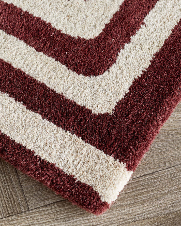 Deep red and cream wool rug with sculpted chevron pattern, displayed on wood flooring.