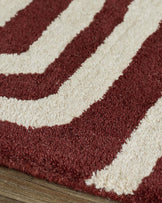 Close-up of deep red and cream wool rug with abstract swirl pattern and sculpted texture on wooden floor.