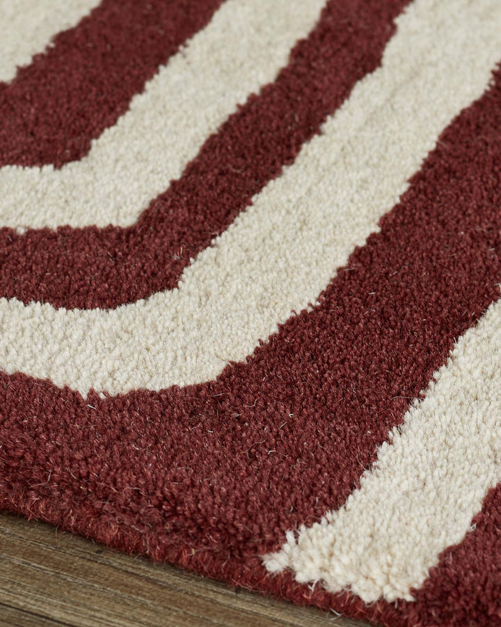 Close-up of deep red and cream wool rug with abstract swirl pattern and sculpted texture on wooden floor.