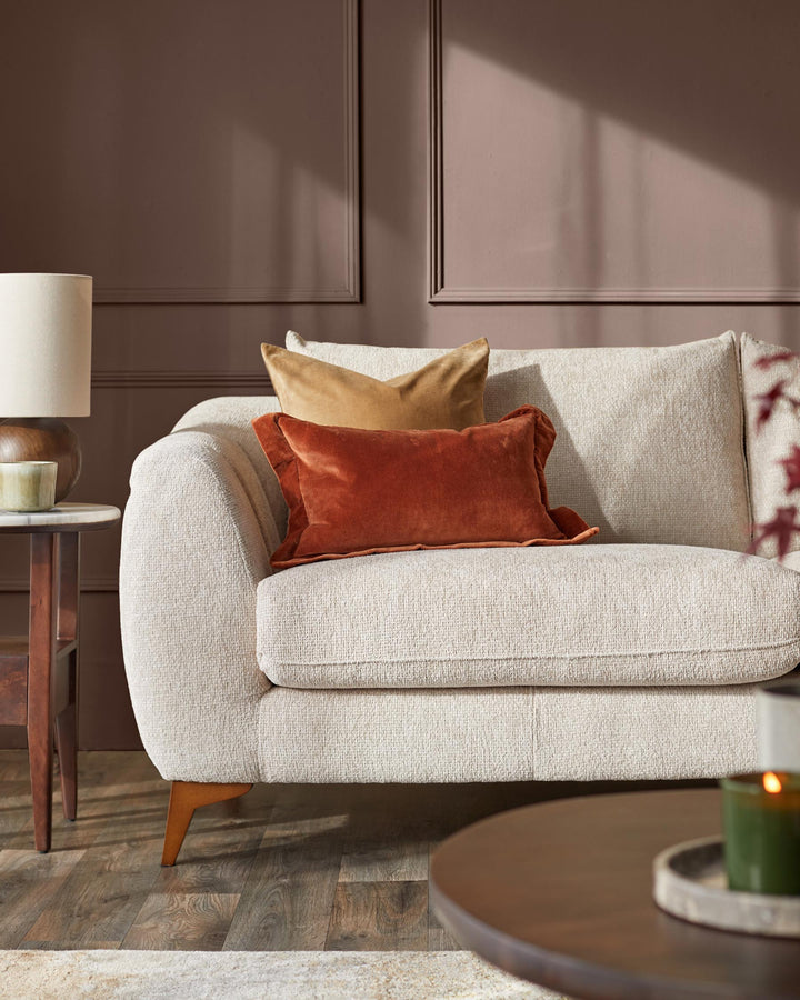A modern sofa with brown and tan pillows sits on a wooden floor. A side table and coffee table are also visible.