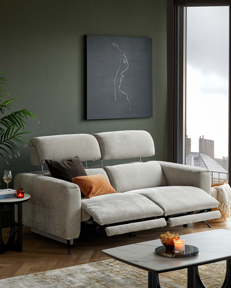 A modern, light gray reclining sofa with decorative cushions, paired with a round black side table and a cozy rug.
