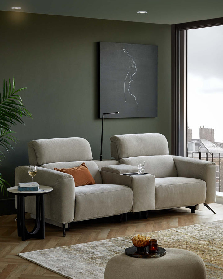A plush grey sofa with a matching side table, accented with a cushion, against a green wall and contemporary art.