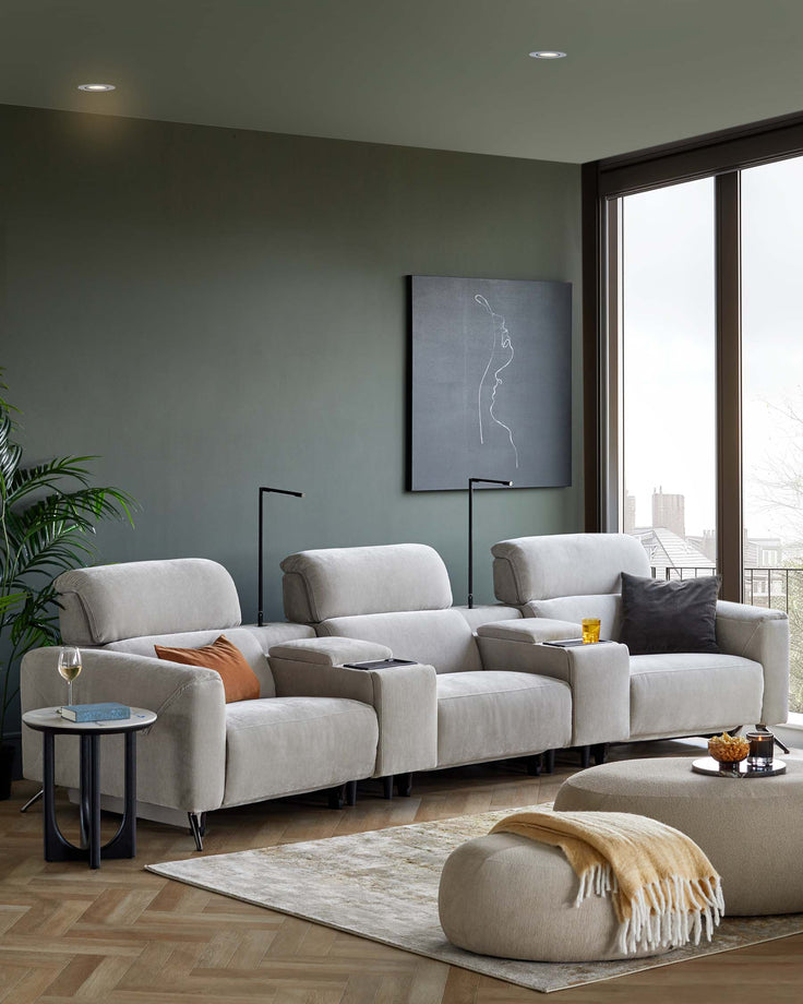 Modern grey reclining sofa, circular ottoman, side table with a drink, and a cozy throw blanket on a textured rug.