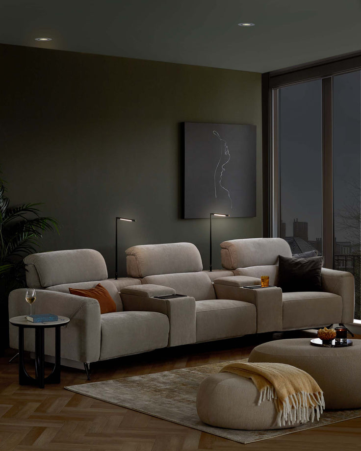 Cozy beige sectional sofa with plush cushions, side tables, and a round pouf, accented by stylish lamps and artwork.