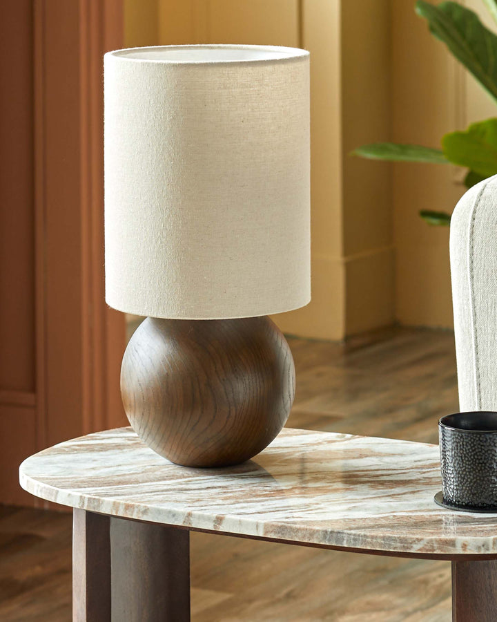 Lamp with wood base and cylindrical shade on a marble-effect table. Neutral colours give a contemporary feel.