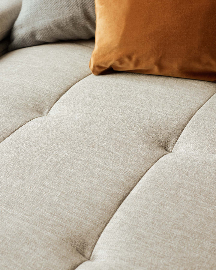 Close-up of a beige fabric sofa with button detailing and cushions. Soft and comfortable seating.